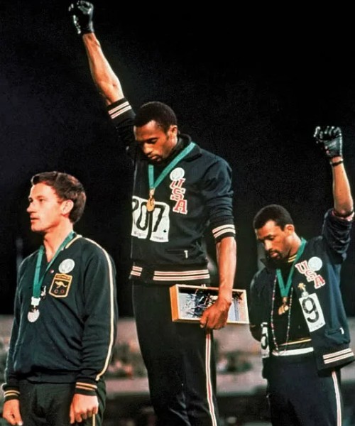 Tommie Smith e John Carlos fazem o protesto com o gesto do grupo Panteras Negras, no pódio dos 200 m nos Jogos de 1968 (Crédito: Reprodução)